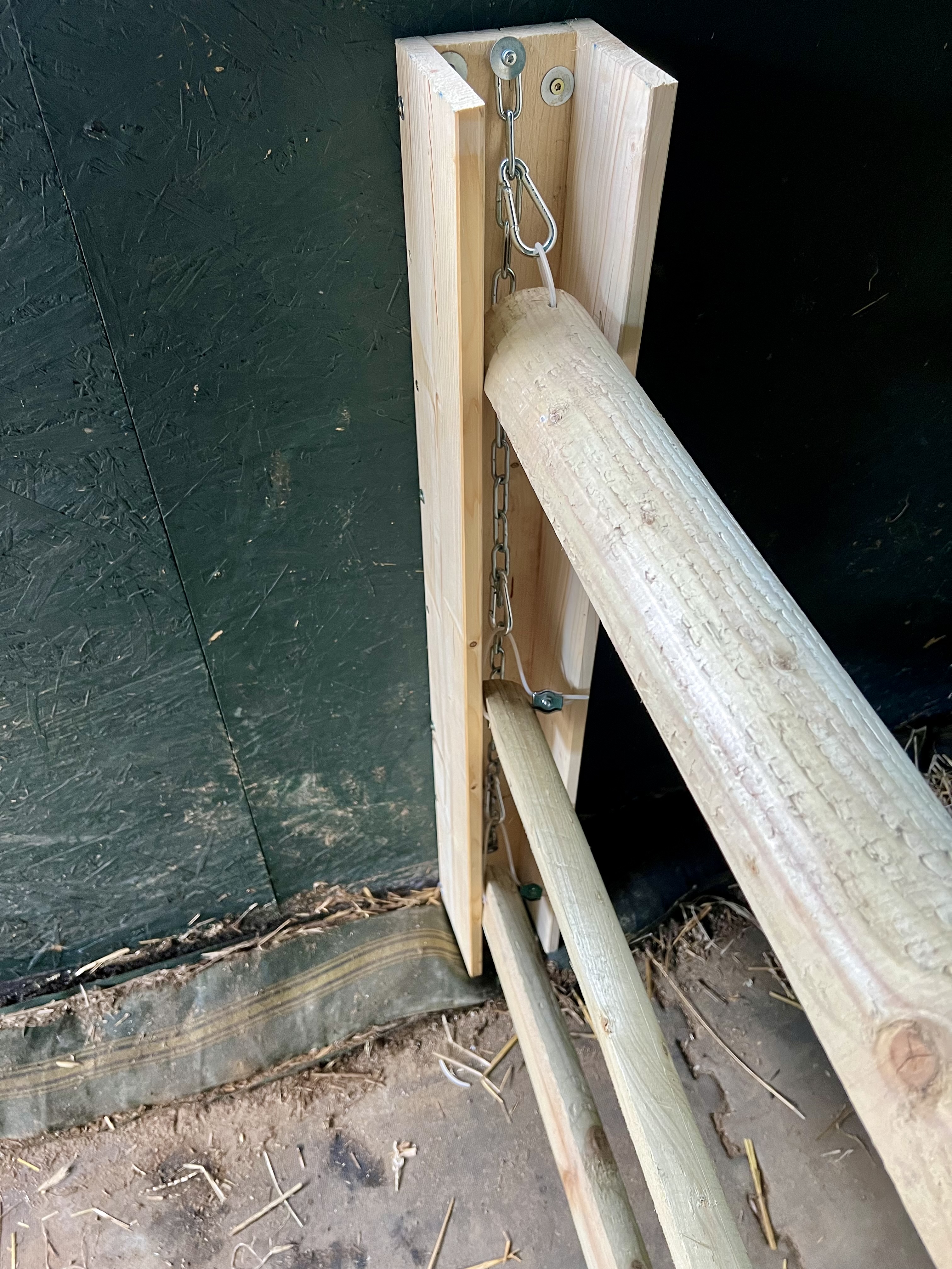 Detailansicht: Karabiner und Rundstahlkette an der Holzlatte der Trennwand